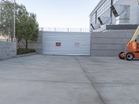 a concrete area with a crane in the middle of it and a building with a gate on the wall behind