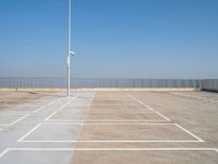 a empty parking lot with an antenna on top and blue sky above it, next to some metal fences