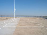 a empty parking lot with an antenna on top and blue sky above it, next to some metal fences