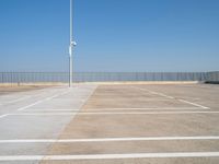 a empty parking lot with an antenna on top and blue sky above it, next to some metal fences