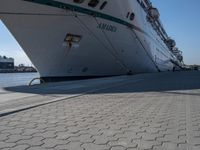 large cruise boat parked in the harbor with people walking by it and water on the pavement