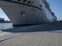 large cruise boat parked in the harbor with people walking by it and water on the pavement