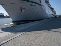 large cruise boat parked in the harbor with people walking by it and water on the pavement