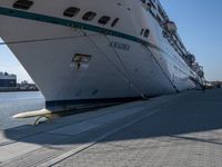 large cruise boat parked in the harbor with people walking by it and water on the pavement