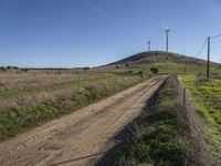 a dirt road passes by several wind turbines on the hillside above the road to the right of it