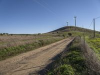 a dirt road passes by several wind turbines on the hillside above the road to the right of it