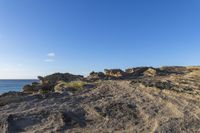 rocky area with grass and rocks on side of body of water in background with blue sky