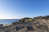 rocky area with grass and rocks on side of body of water in background with blue sky