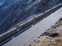 a man riding a motorcycle down the road on a cliff near mountains with snow covered peaks