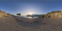 a fisheye lens image of a cliff side road at sunset with an empty bench