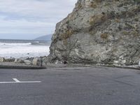 a woman with a surfboard is riding on the road near a cliff side beach