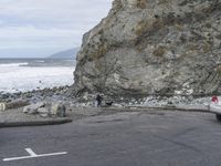 a woman with a surfboard is riding on the road near a cliff side beach