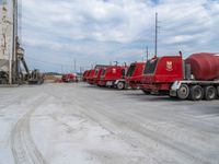 several red trucks parked next to each other at a factory setting with machinery in the back