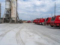 several red trucks parked next to each other at a factory setting with machinery in the back