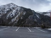 an empty parking lot with snow and a large mountain in the background below it with trees on the side