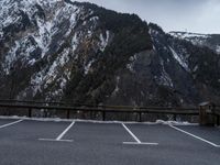 an empty parking lot with snow and a large mountain in the background below it with trees on the side