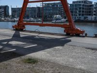 a large red crane in front of buildings on the river bank by the pier and boats