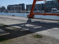 a large red crane in front of buildings on the river bank by the pier and boats