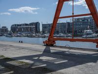 a large red crane in front of buildings on the river bank by the pier and boats