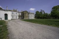 a paved path leading to a large stone building with columns and three green front doors