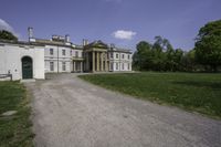 a paved path leading to a large stone building with columns and three green front doors