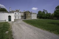 a paved path leading to a large stone building with columns and three green front doors