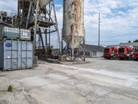 a group of three fire trucks are sitting in a lot next to a tall concrete silo