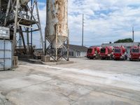 a group of three fire trucks are sitting in a lot next to a tall concrete silo