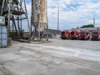 a group of three fire trucks are sitting in a lot next to a tall concrete silo