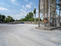 cement tanks are next to a metal plant in a parking lot with trees behind them