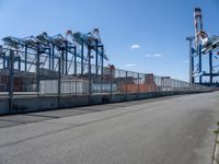 an empty street with lots of containers hanging around it and some cranes in the background