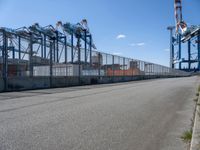 an empty street with lots of containers hanging around it and some cranes in the background