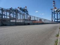 an empty street with lots of containers hanging around it and some cranes in the background