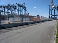 an empty street with lots of containers hanging around it and some cranes in the background