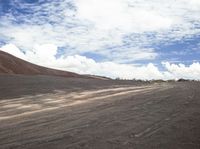 a man walking on a road with some gravel and some clouds in the sky and hills