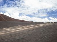 a man walking on a road with some gravel and some clouds in the sky and hills