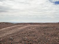 an arid land with red dirt and rocks and one orange fire hydrant and some white clouds