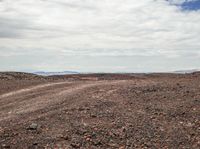 an arid land with red dirt and rocks and one orange fire hydrant and some white clouds