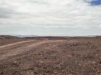 an arid land with red dirt and rocks and one orange fire hydrant and some white clouds