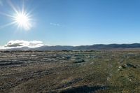 view of rocky area in open area with sunny sky and mountains behind it and clear blue sky