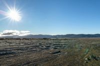 view of rocky area in open area with sunny sky and mountains behind it and clear blue sky