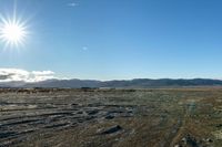 view of rocky area in open area with sunny sky and mountains behind it and clear blue sky