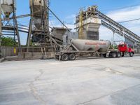 a red dump truck is parked near concrete mills and grain silos in the background