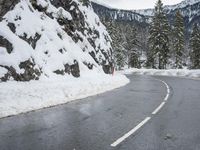 a curved road is covered in snow near a large mountain side in the winter snow