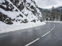 a curved road is covered in snow near a large mountain side in the winter snow