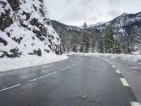 a curved road is covered in snow near a large mountain side in the winter snow