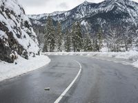 a curved road is covered in snow near a large mountain side in the winter snow