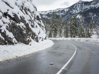 a curved road is covered in snow near a large mountain side in the winter snow