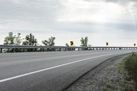 a paved road with yellow traffic signs on the side and trees in the background on a cloudy day