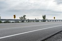 a paved road with yellow traffic signs on the side and trees in the background on a cloudy day